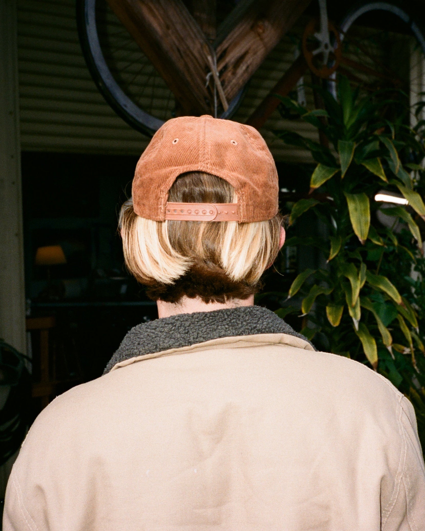 Person wearing a brown cap in an outdoor setting with plants and a bicycle.