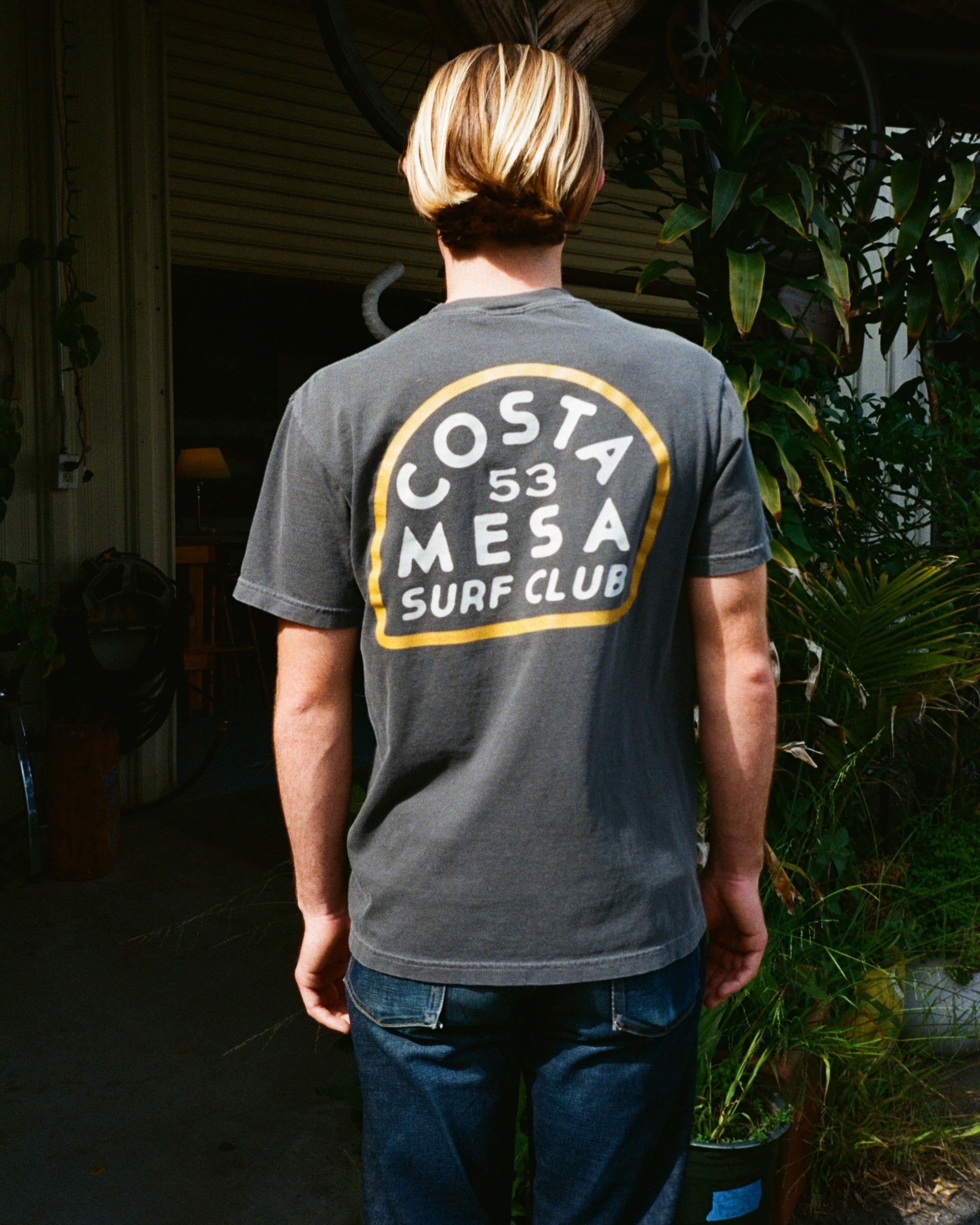 Person wearing a 'Costa Mesa Surf Club' t-shirt with a scenic background