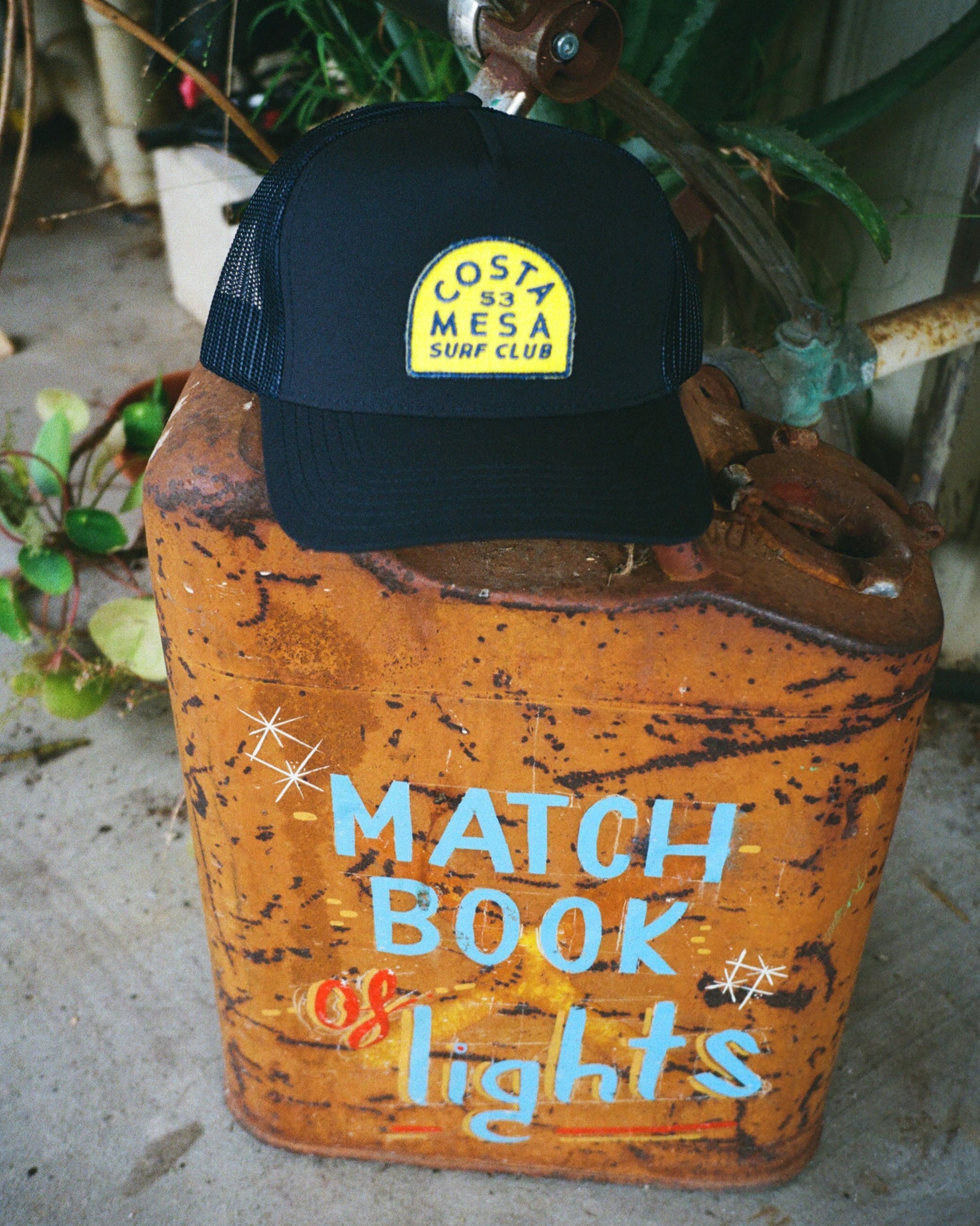 Rust-covered matchbook container with a blue cap featuring a logo on a concrete surface.