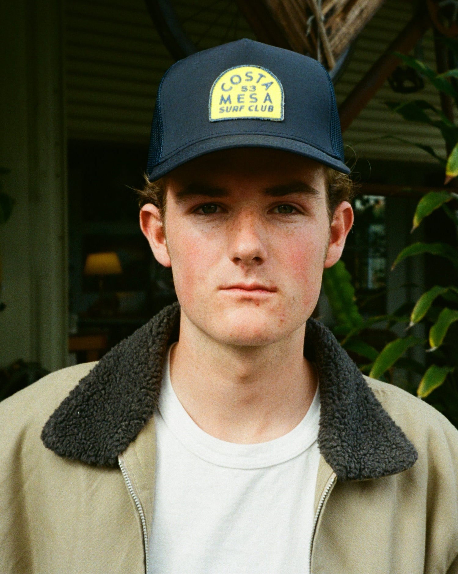 Person wearing a cap and jacket outdoors with plants in the background