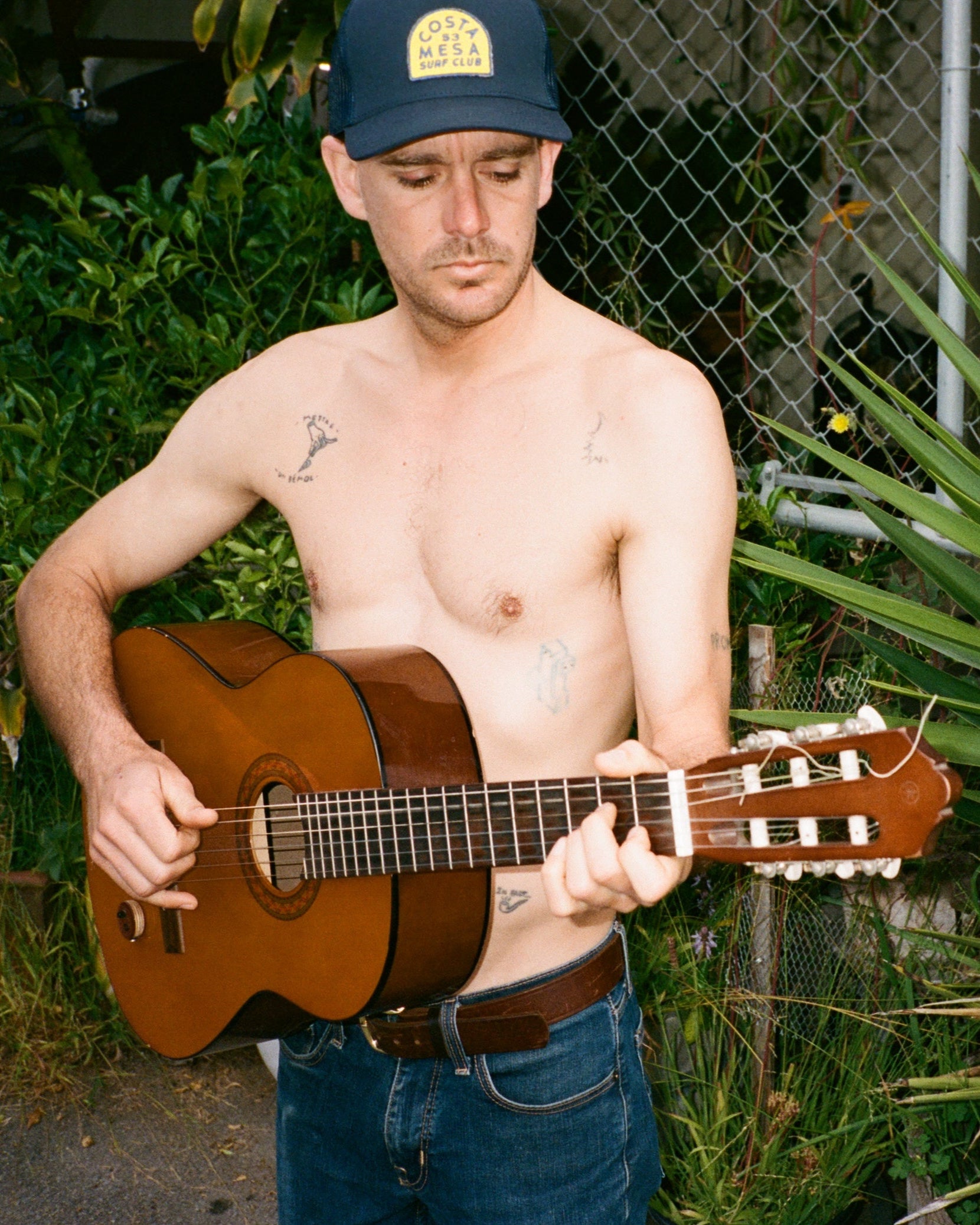 Man playing a guitar outdoors with plants in the background