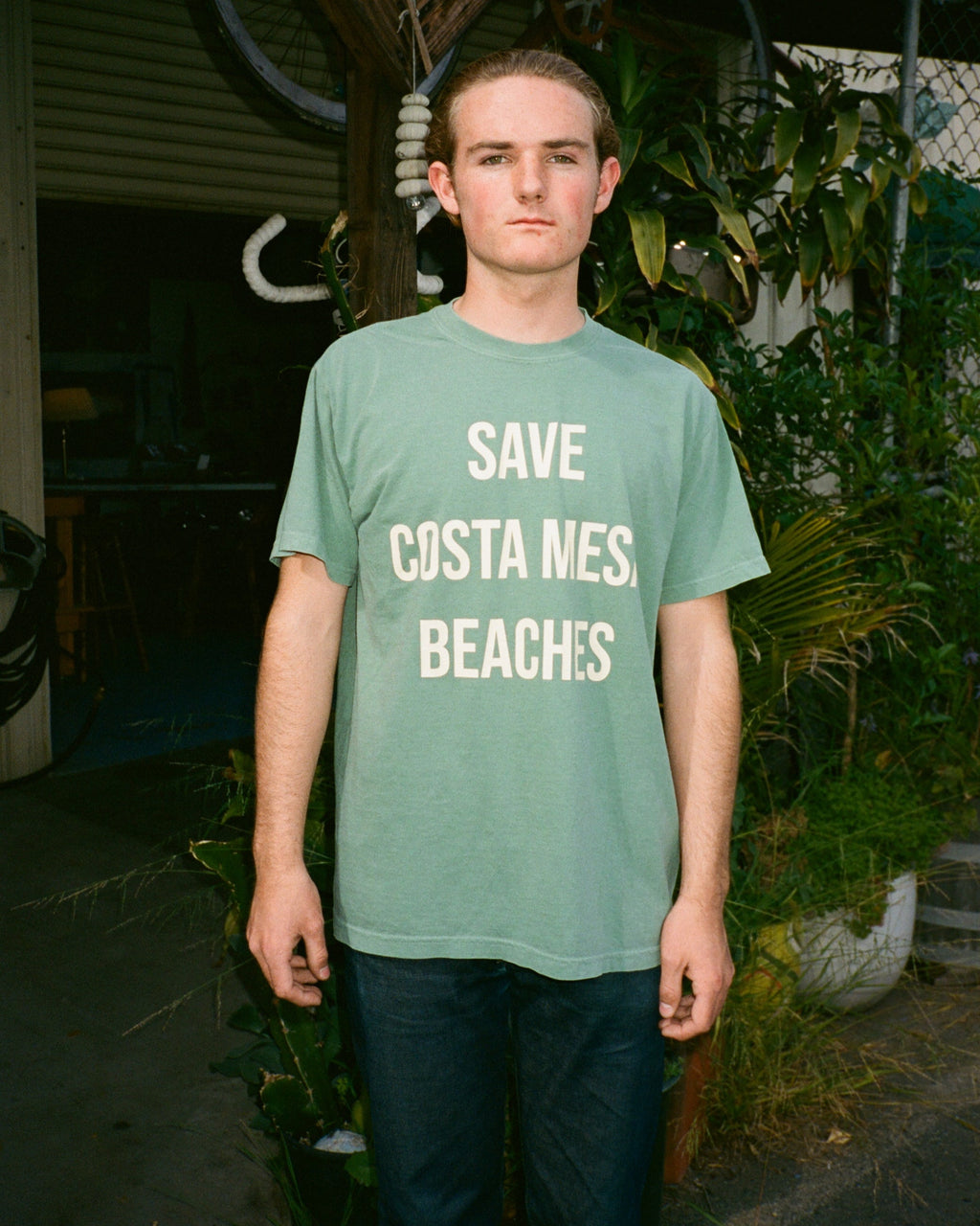 Person wearing a green t-shirt with 'Save Costa Mesa Beaches' text in an outdoor setting.